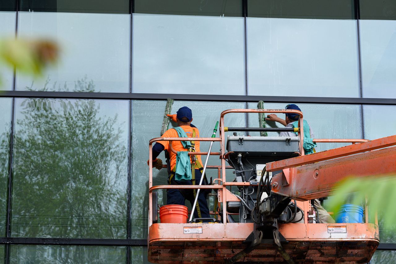 heros-img Two workers cleaning windows on a glass building facade using a lift platform, enhancing building aesthetics.